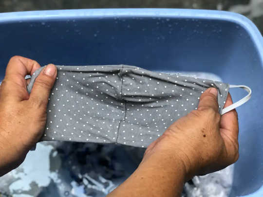 A person washing their mask in a bucket with water and deterganet