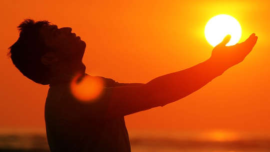 man outside with hands outstretched to the sun