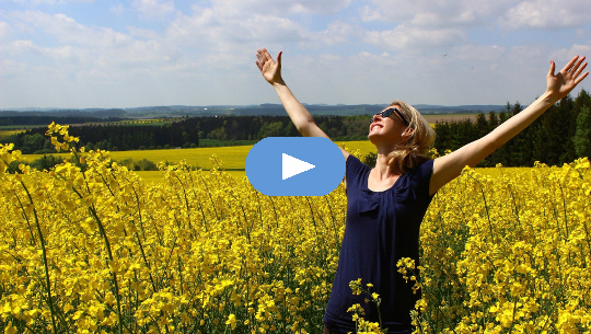 woman standing in a field of flowers with arms upstretched to the sun