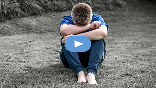 boy sitting on the sand with his head on his knees