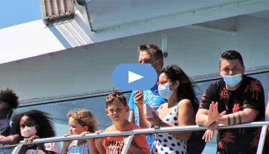 people, most wearing masks, standing on the railing of a cruise ship