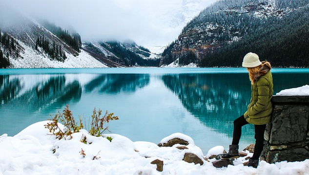 young woman standing in the snow next to a lake