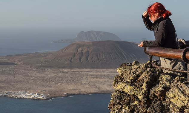 a woman standing  behind the guard-rail at a stone lookout, looking out into the distance