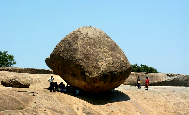 people sitting in the shade of a huge rock 