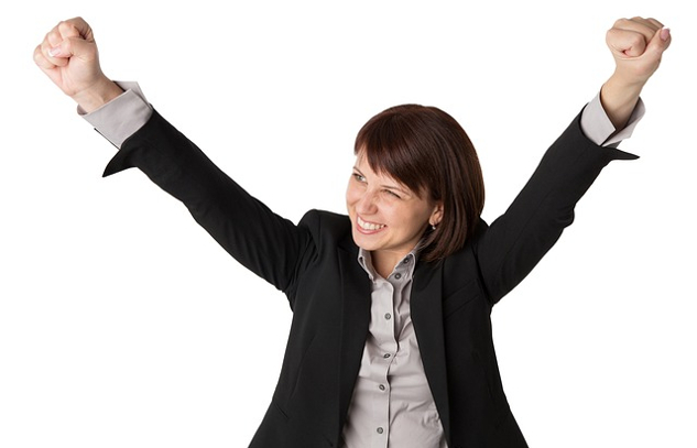 woman with a huge smile, wearing a suit, and with her arms up in the air in victory