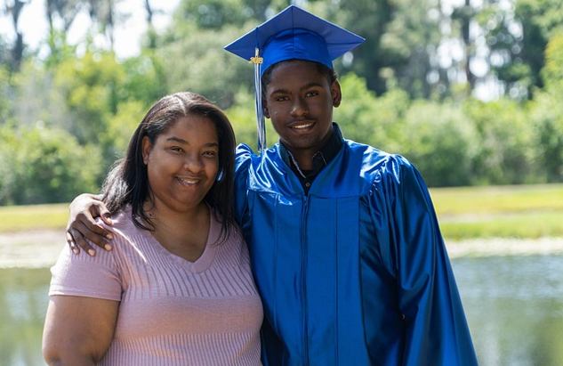 a young black man, wearing his graduation cap and robe, has his arm around his smiling mother's shoulders