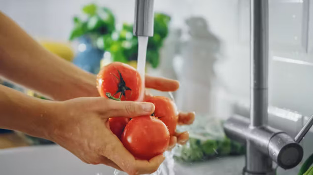 Fresh fruits and vegetables being washed under cold running water to remove dirt, bacteria, and pesticides.