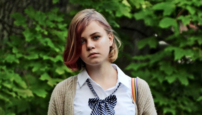 young teen with dyed-pink bangs looking sad outdoors