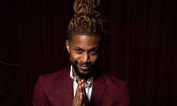 a man, with his dreadlocks tied up in a bun on top of his head, wearing a burgundy suit