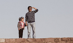 a father and daughter standing on a stone wall with the father looking into the distance