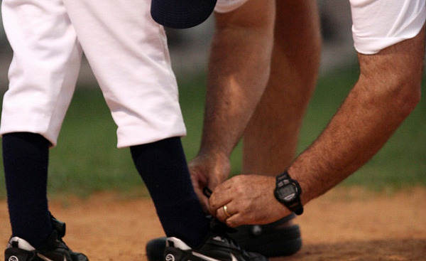 coach tying the shoe of a baseball player