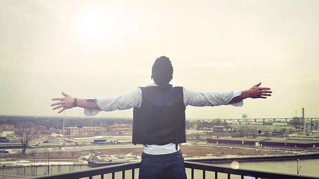 man standing looking out from a balcony with his arms wide open to the horizon