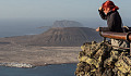 a woman standing  behind the guard-rail at a stone lookout, looking out into the distance