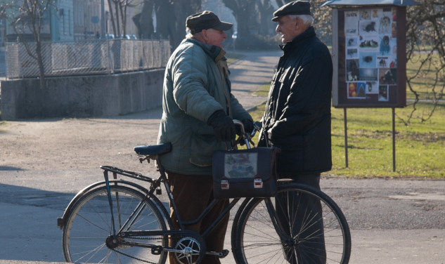 two older men speaking in the street, one is standing next to a bicycle