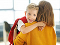 Child walking into school with backpack, smiling parent waving goodbye, representing a positive start to primary school.