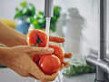 Fresh fruits and vegetables being washed under cold running water to remove dirt, bacteria, and pesticides.