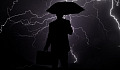 a businessman holding an umbrella over his head and facing a black sky filled with lightning